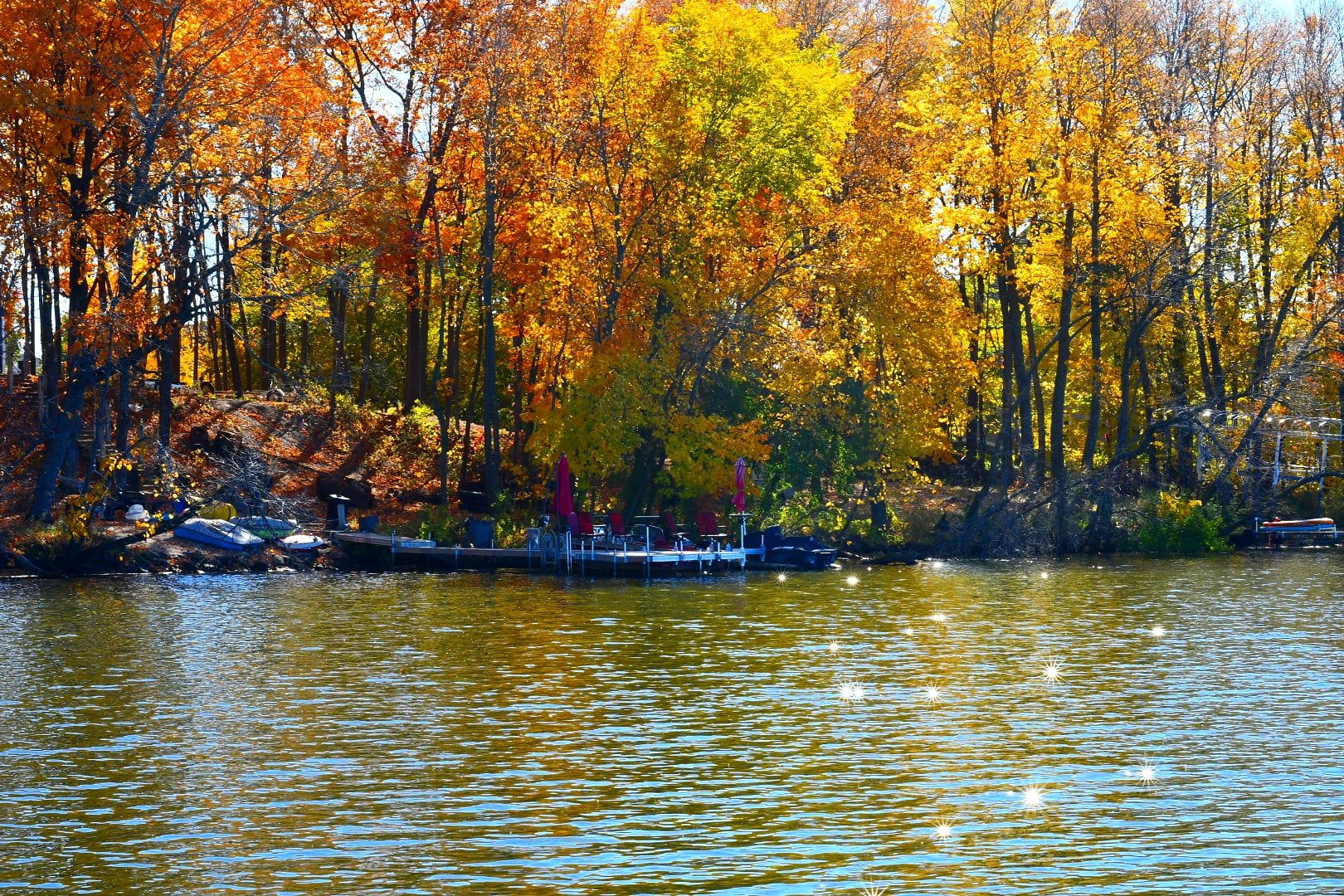 Colorful fall foliage reflects in calm lake waters on a sunny autumn day.