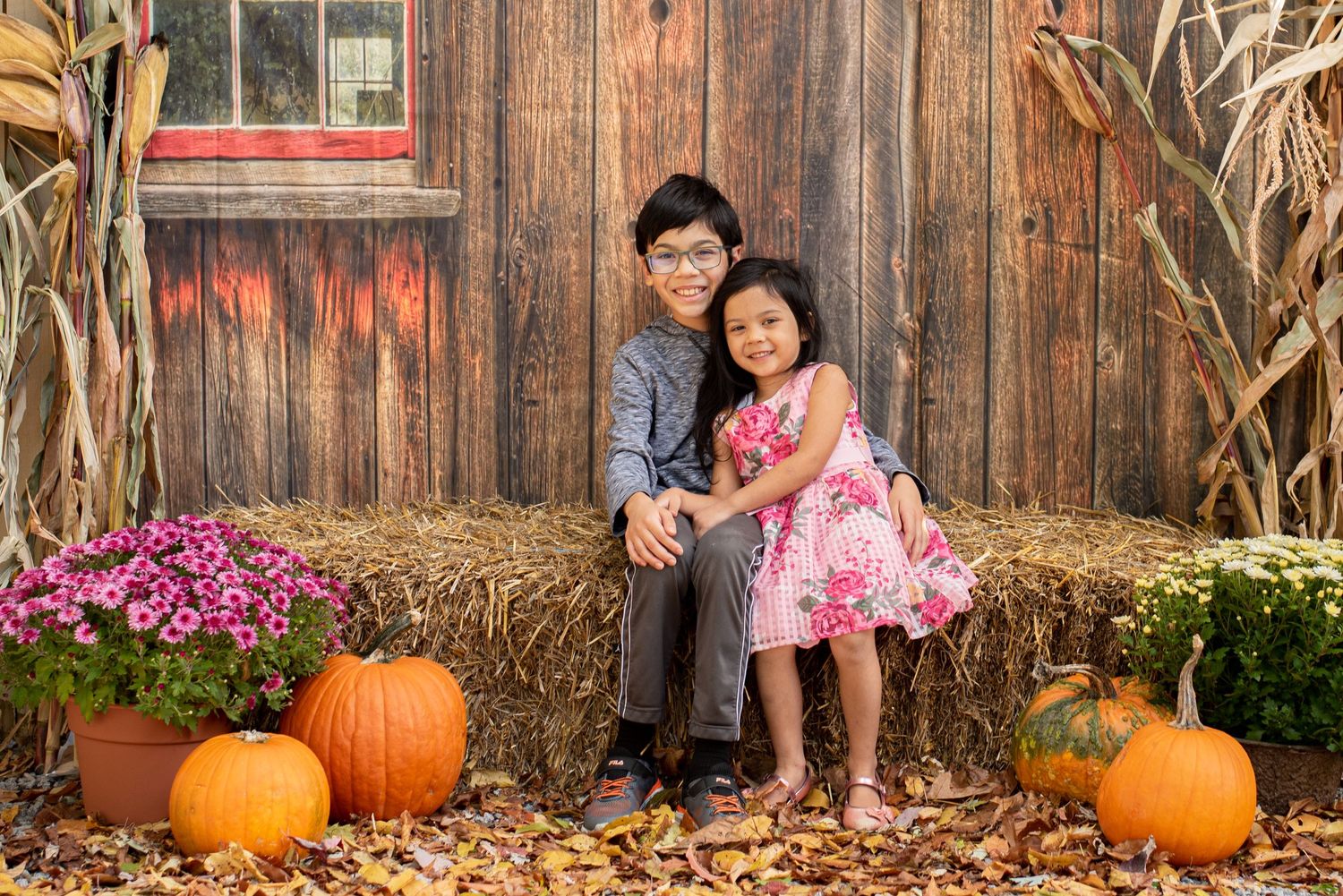siblings sitting on hay bale for fall mini session with pumpkins