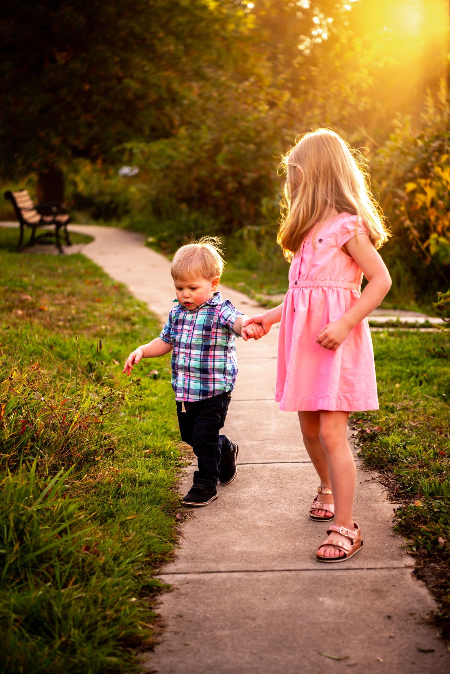 sister and brother holding hands on a path near north park lake at sunset