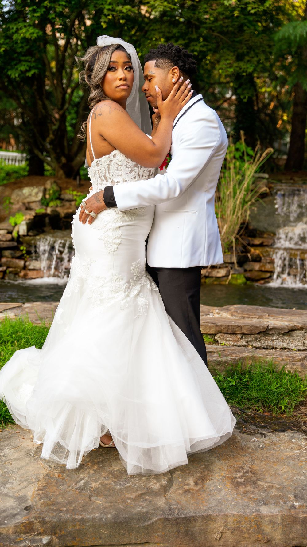 Wedding couple poses by waterfall in elegant white attire.
