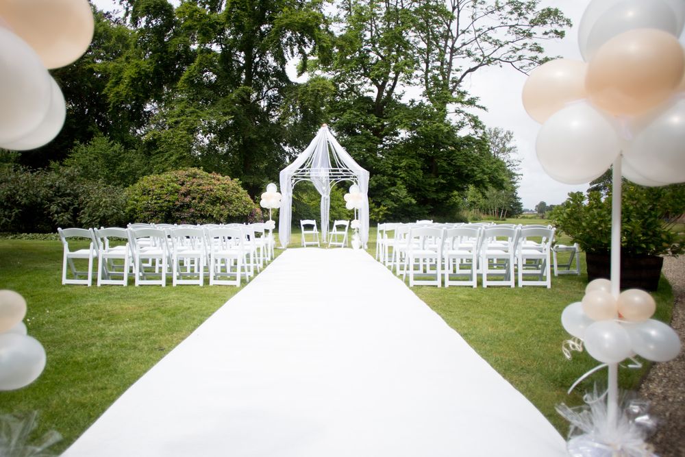 Outdoor wedding ceremony setup with white aisle runner, chairs and gazebo.