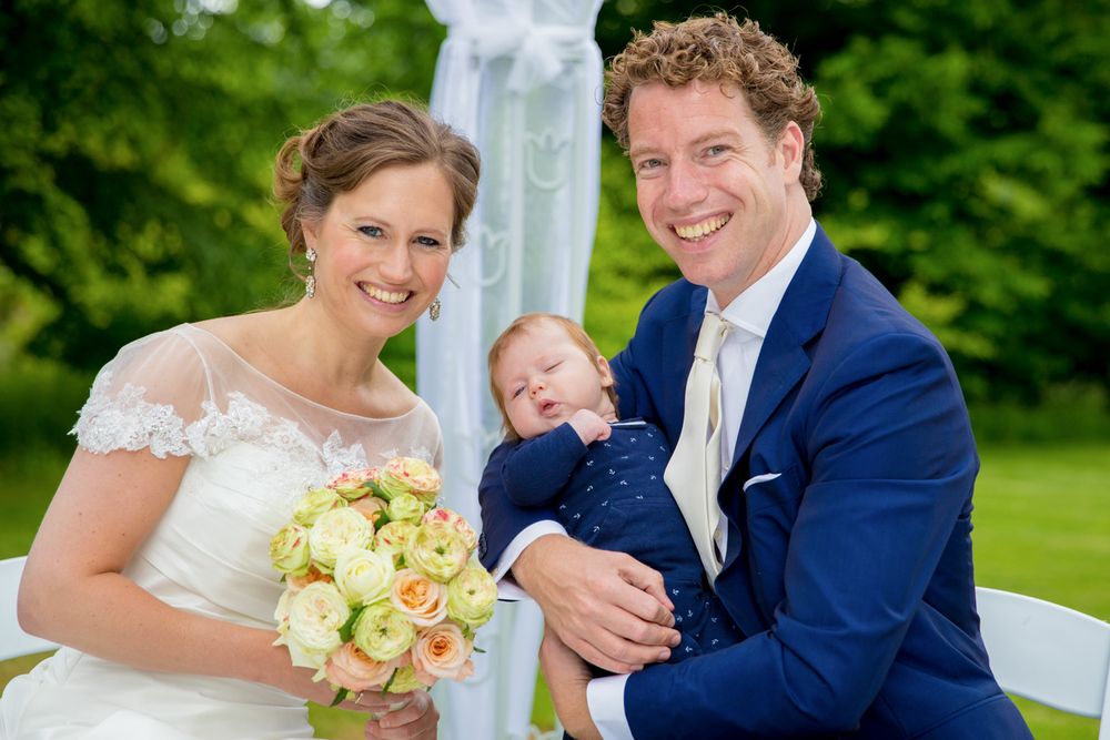 Wedding couple poses with infant at outdoor garden ceremony.