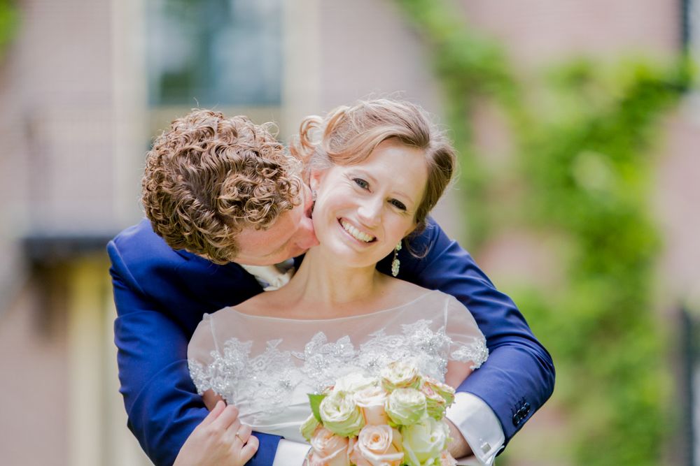 Candid moment of newlyweds sharing a joyful embrace while holding a pastel bouquet.