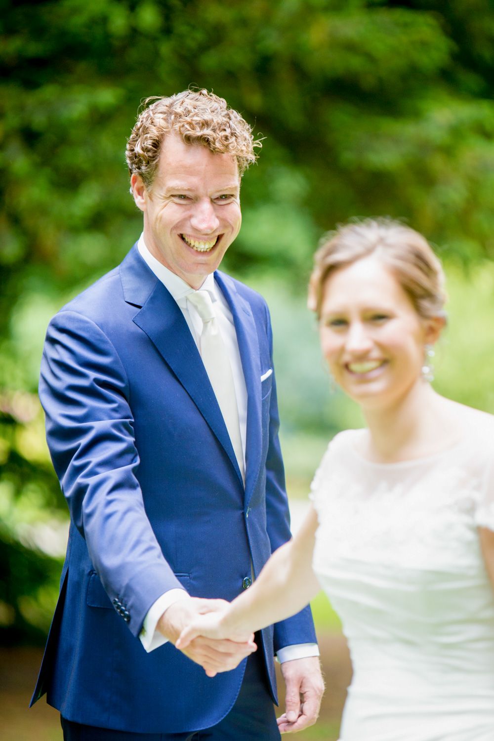 Joyful outdoor wedding portrait with natural greenery backdrop.