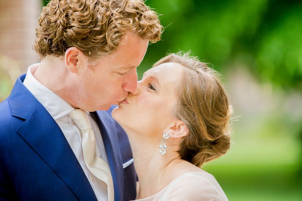 Tender wedding kiss captured in natural outdoor setting.