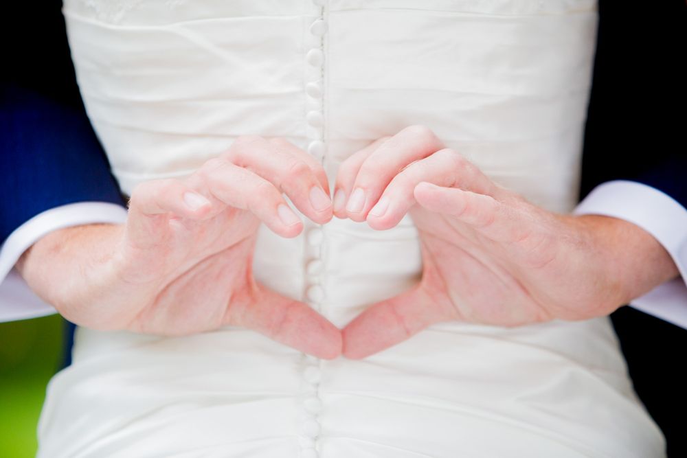 Hands form a heart shape against white wedding dress.