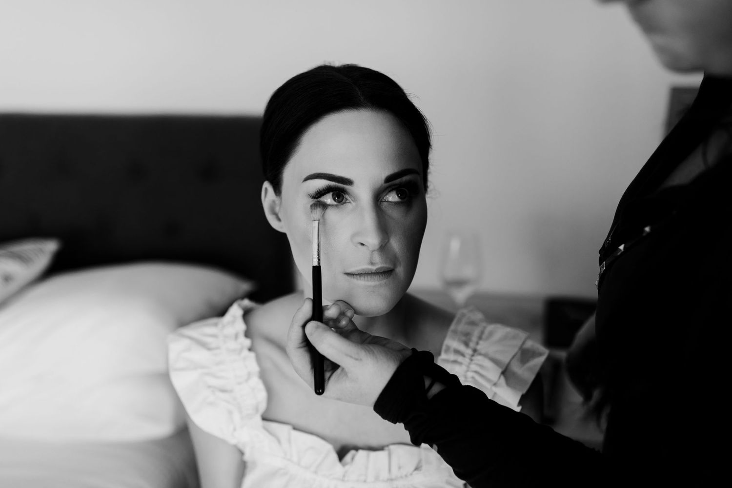 Black and white close-up portrait showing makeup application during bridal preparation.