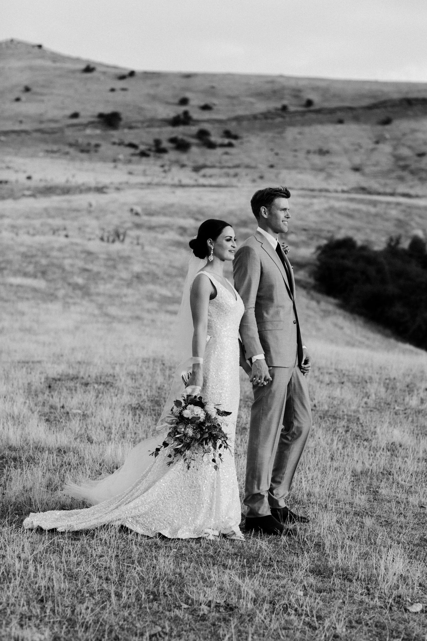 Black and white wedding portrait of couple standing in dramatic hillside landscape.