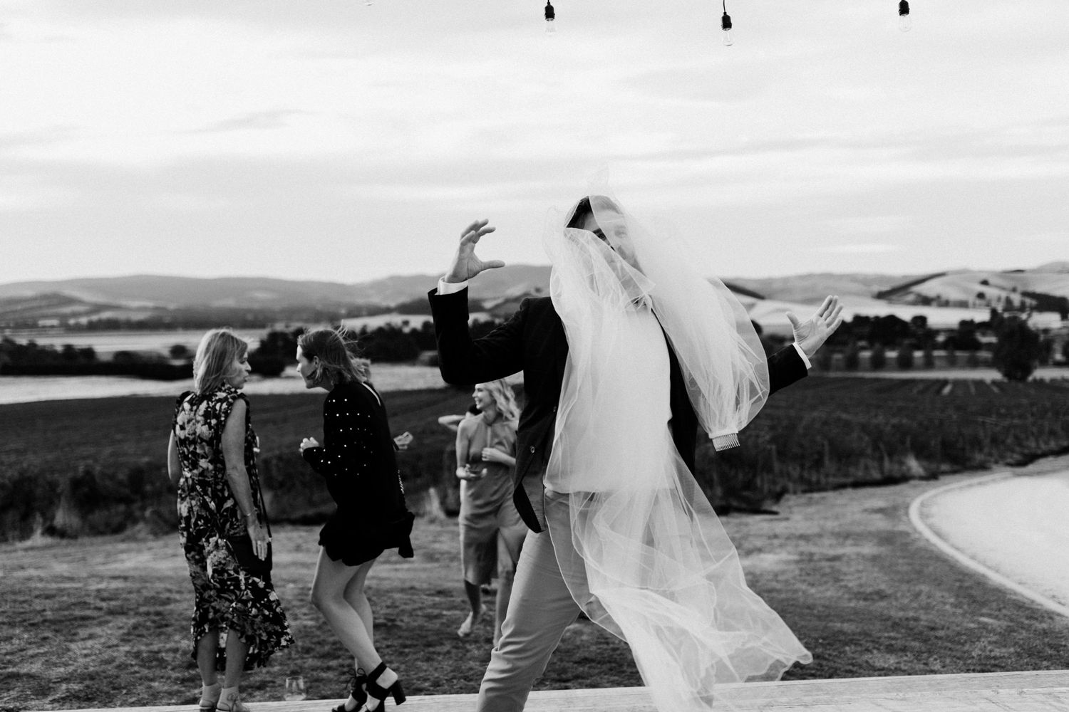 Wedding party dancing and celebrating outdoors with flowing veil in the wind.