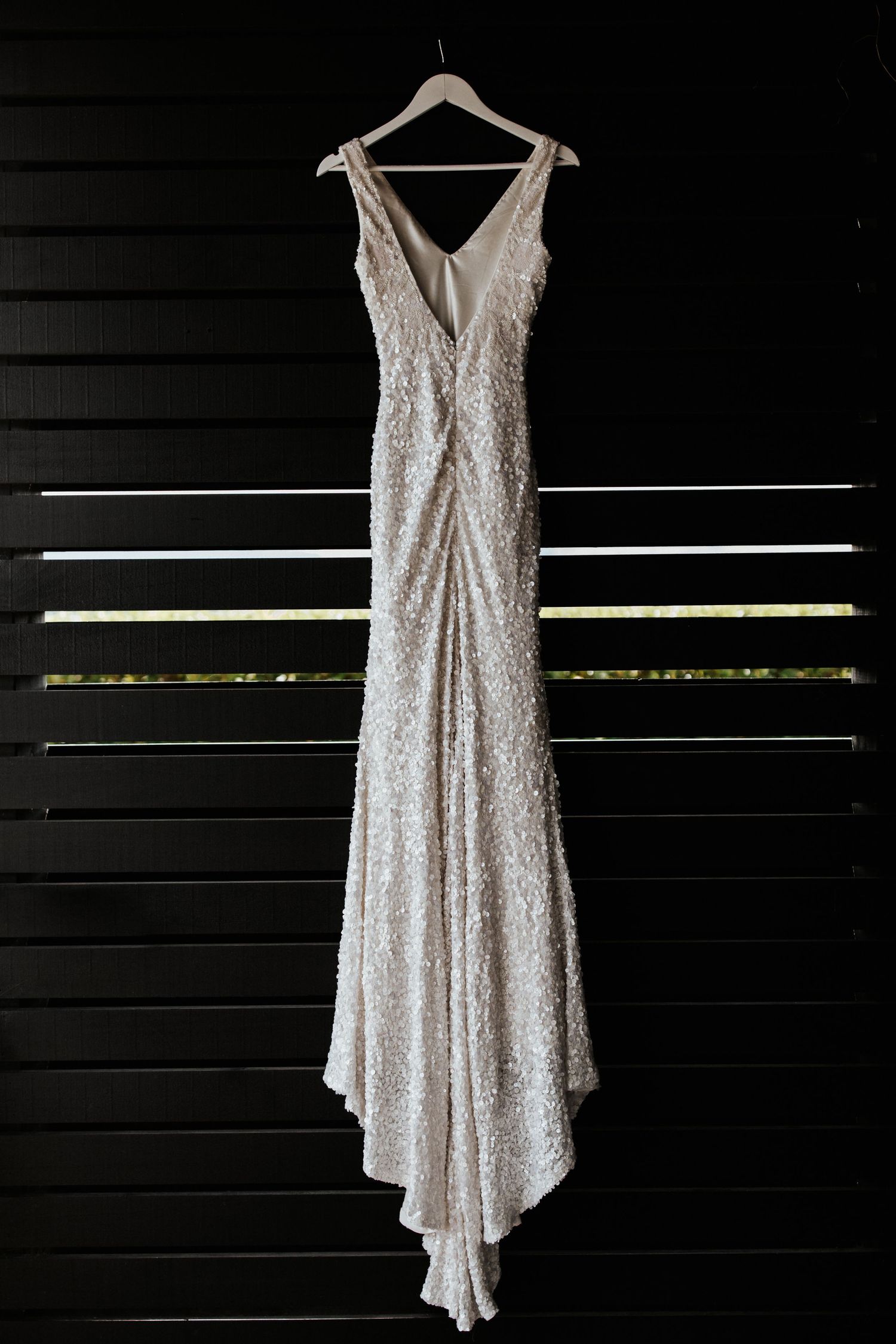 Elegant white sequined wedding dress with plunging neckline hanging against dark wall.