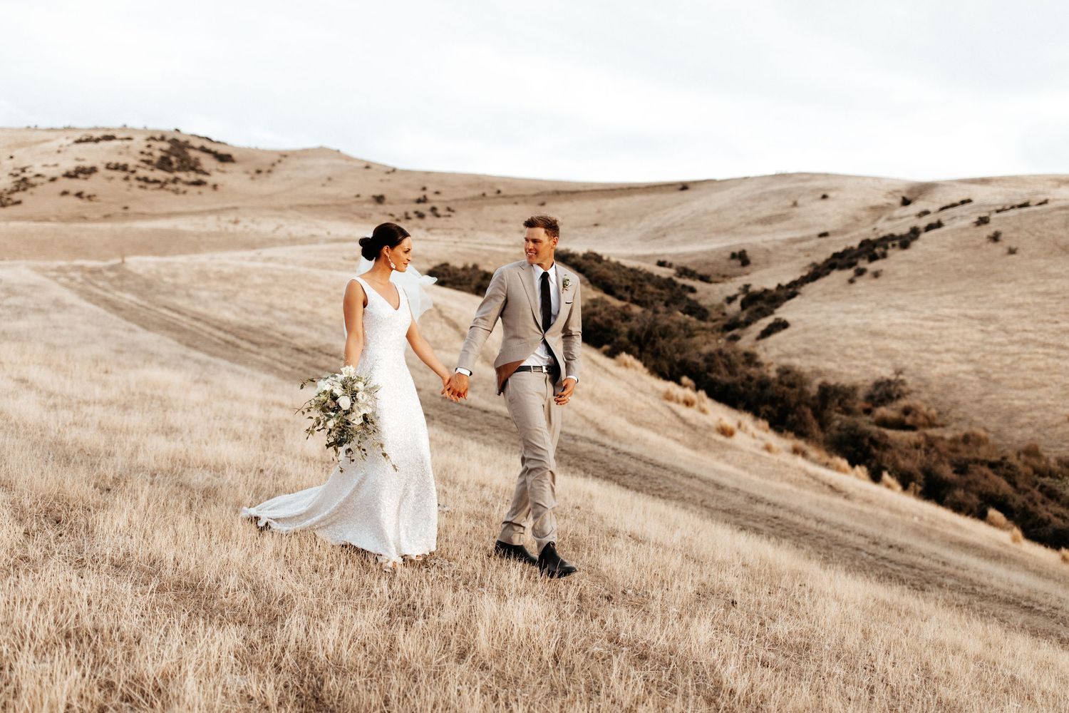 Newlyweds share a moment on a hilltop overlooking rolling pastoral landscape.