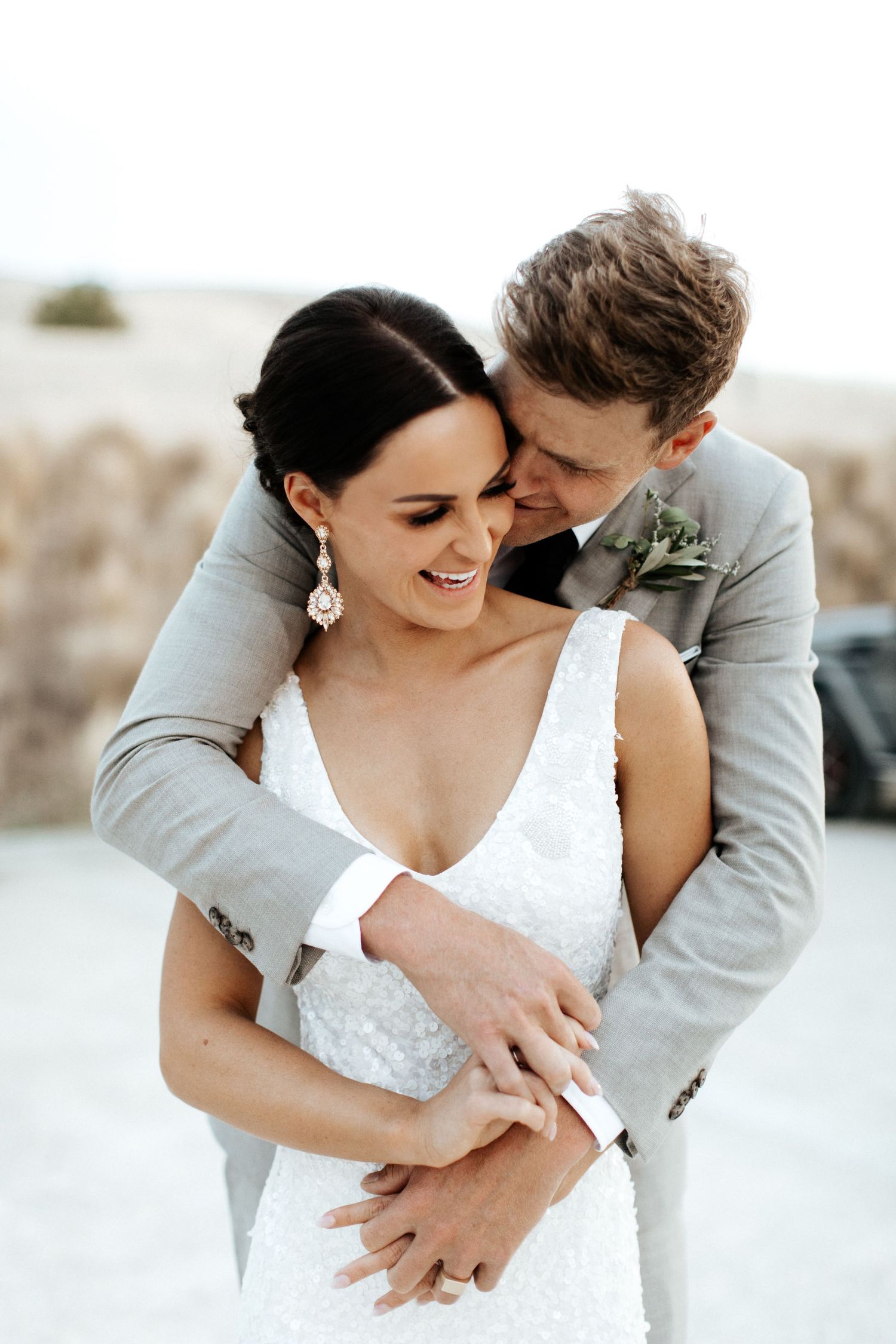 Tender wedding moment captured as couple embraces in formal attire against neutral background.