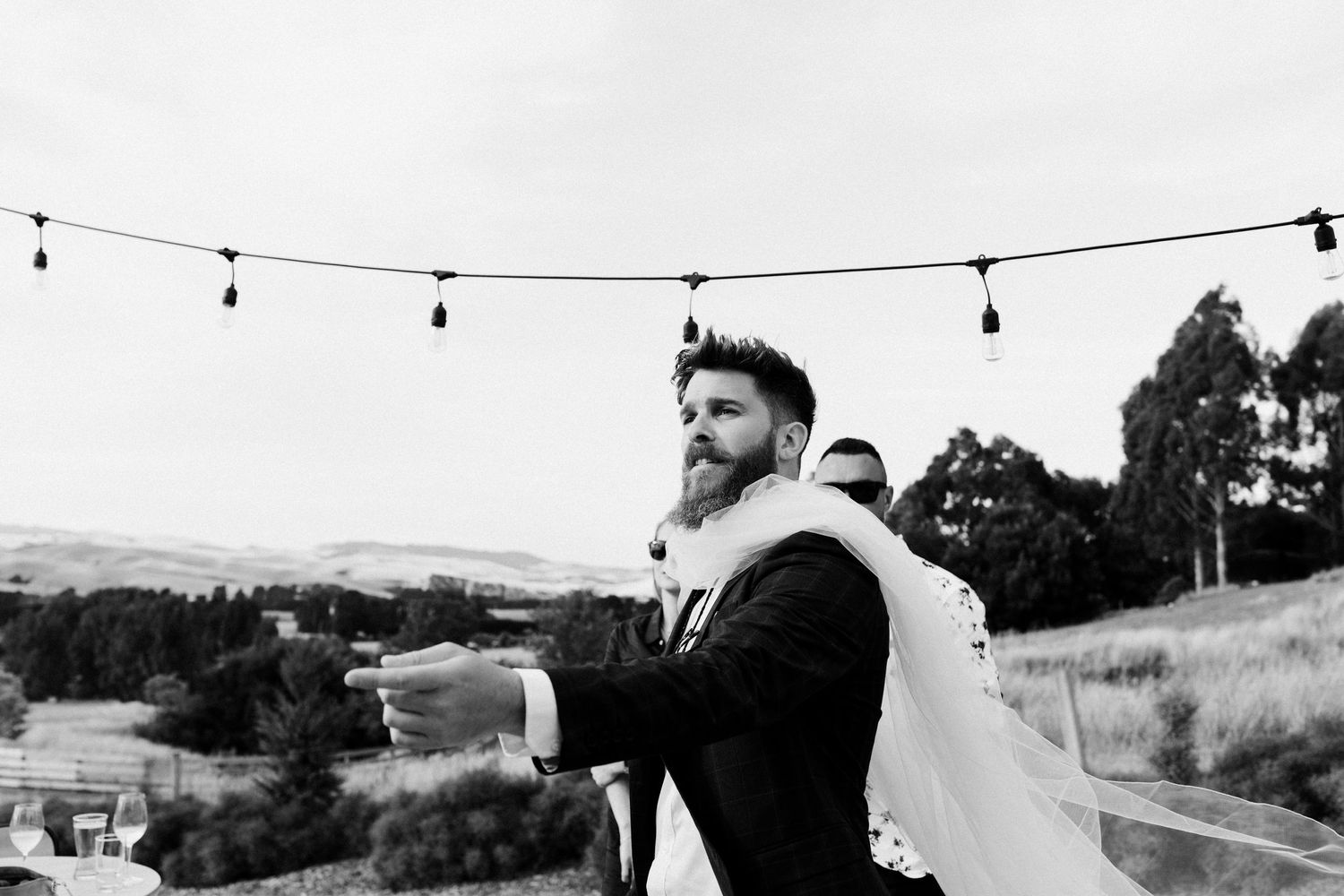Wedding couple shares a moment under string lights at an outdoor venue with mountain views.