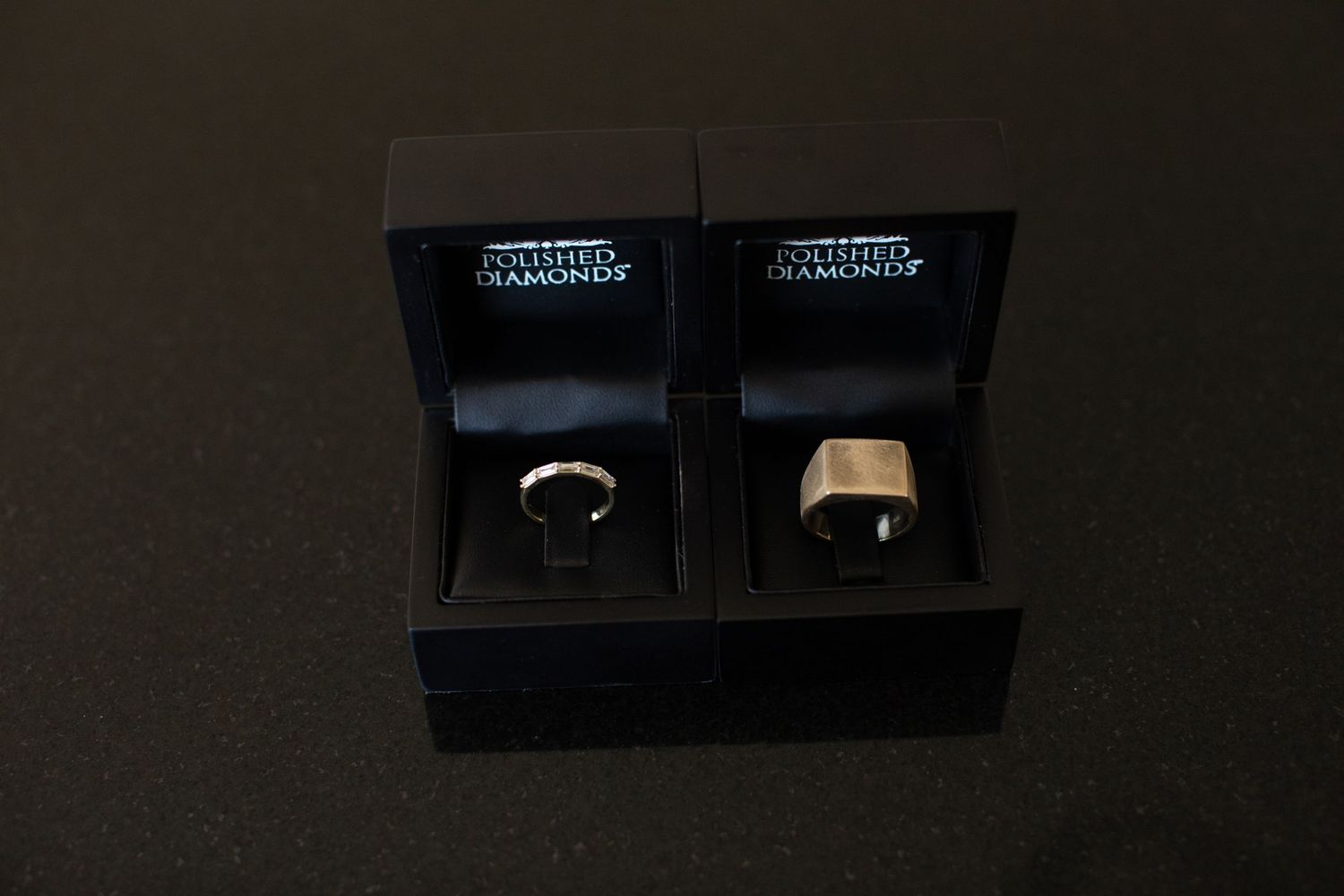 Two wedding rings displayed in elegant black jewelry boxes against a dark background.