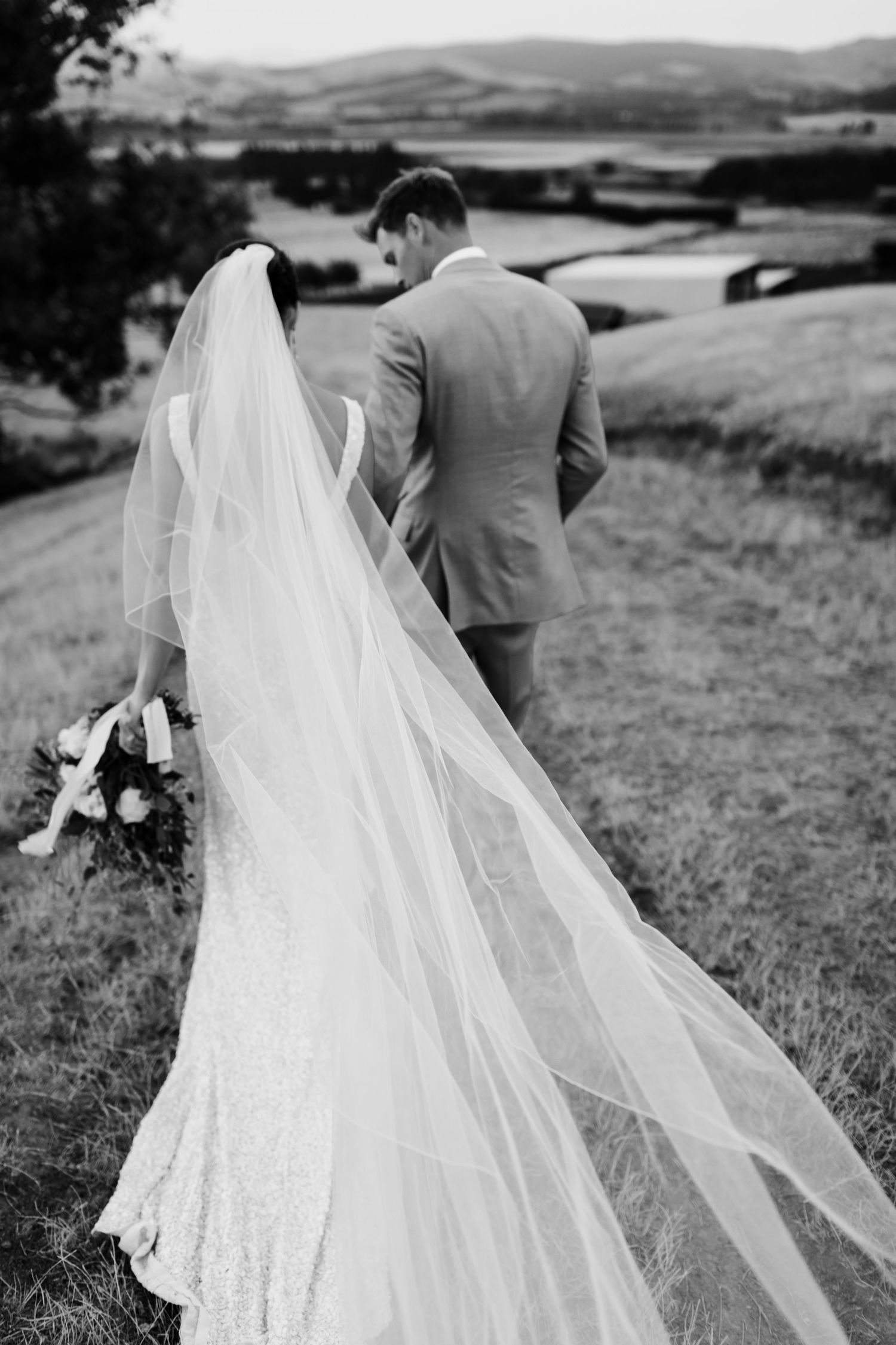 Dramatic black and white photo showing bride's long veil flowing in wind on mountainside.