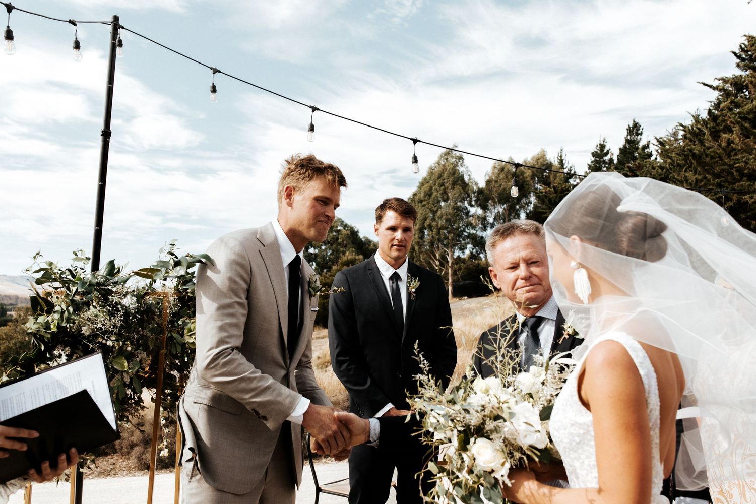 Outdoor wedding ceremony with couple exchanging vows under string lights.