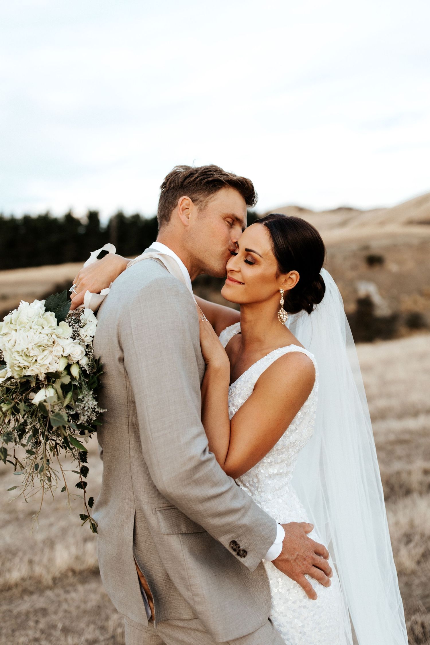 Romantic wedding portrait of newlyweds embracing against a scenic mountain backdrop.