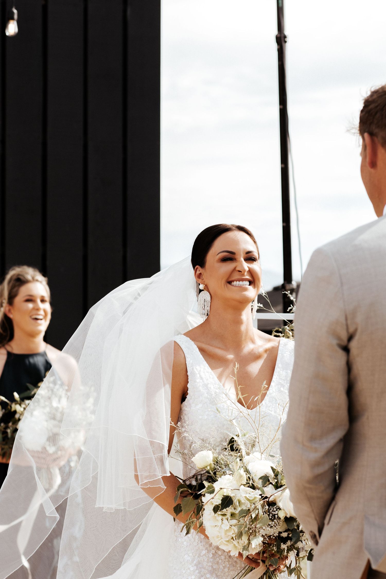 A joyful outdoor wedding ceremony moment as the bride laughs while holding a white bouquet.