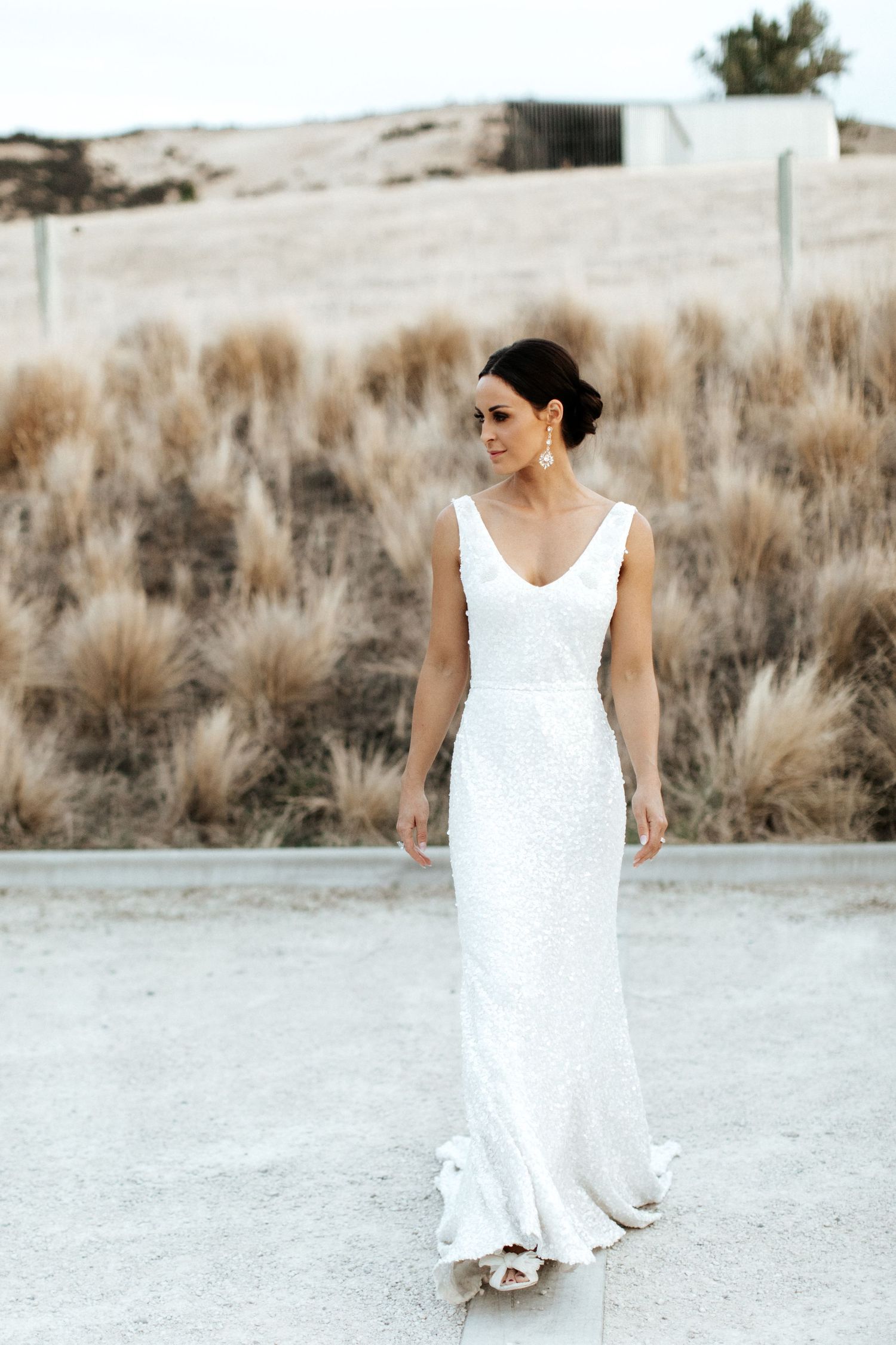 Bride in fitted white v-neck wedding gown stands elegantly against desert landscape.