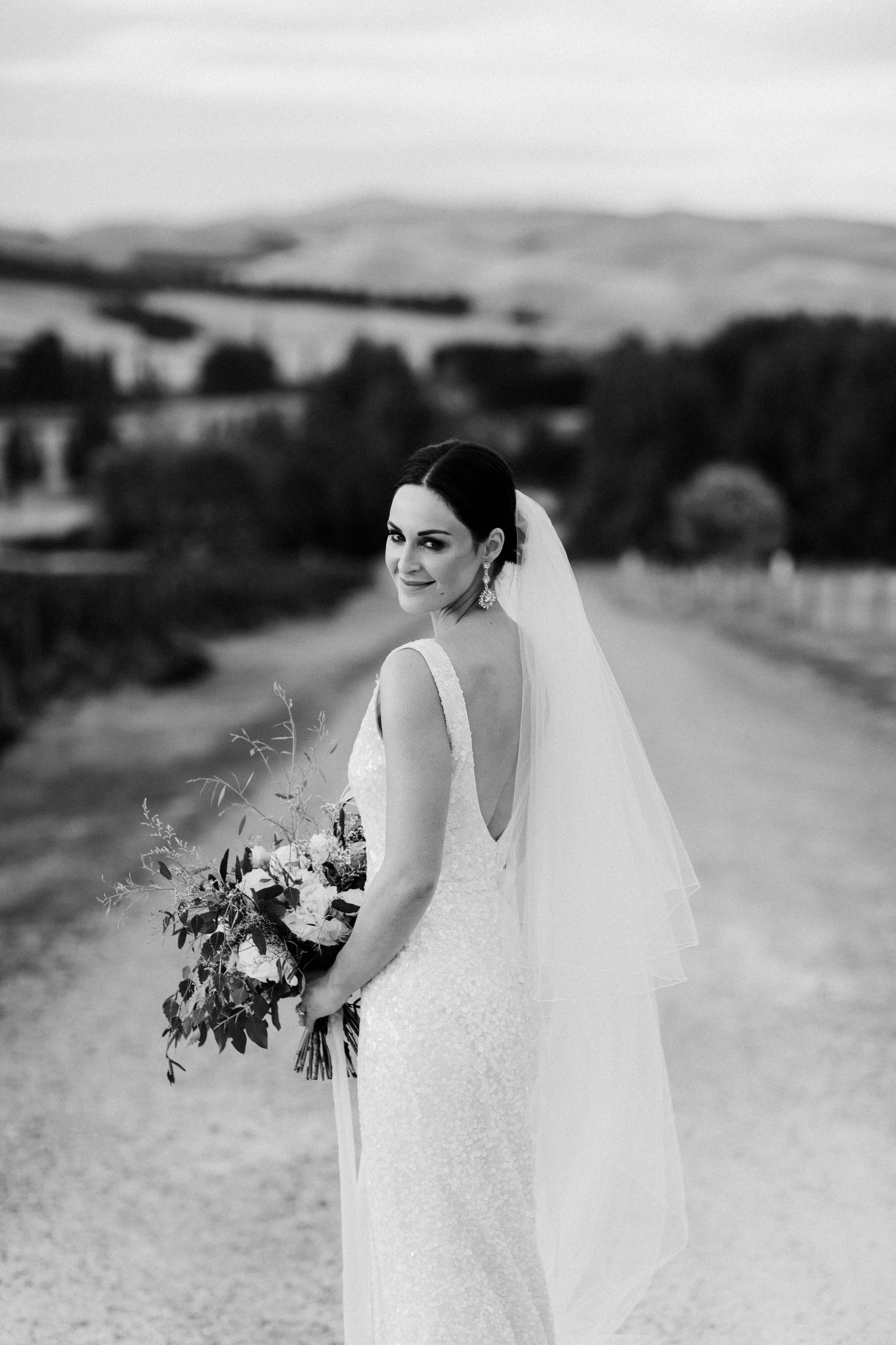 Black and white portrait of bride holding bouquet on country path with scenic view.