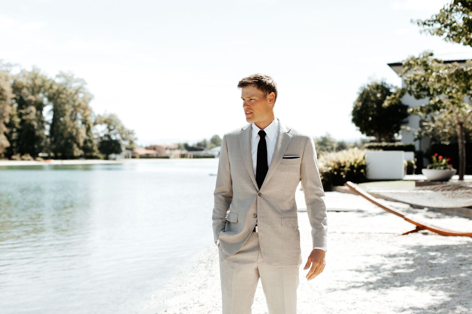 Person in a light suit standing by a waterfront on a bright sunny day.