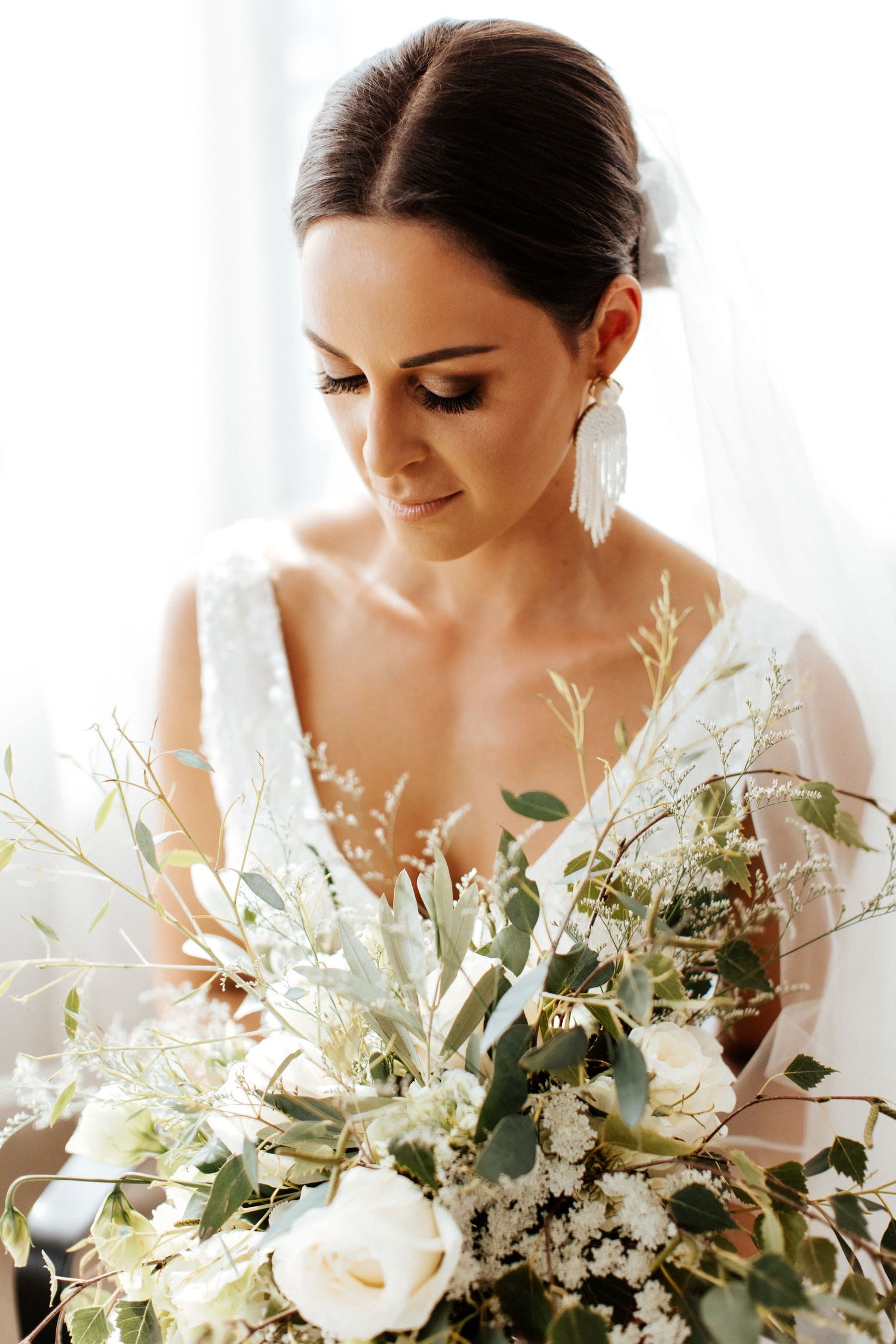 Bride holding a romantic white and green bouquet in natural window light.