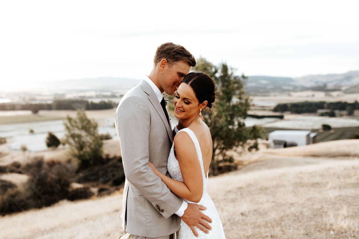 Tender embrace between newlyweds on hilltop with scenic valley views.