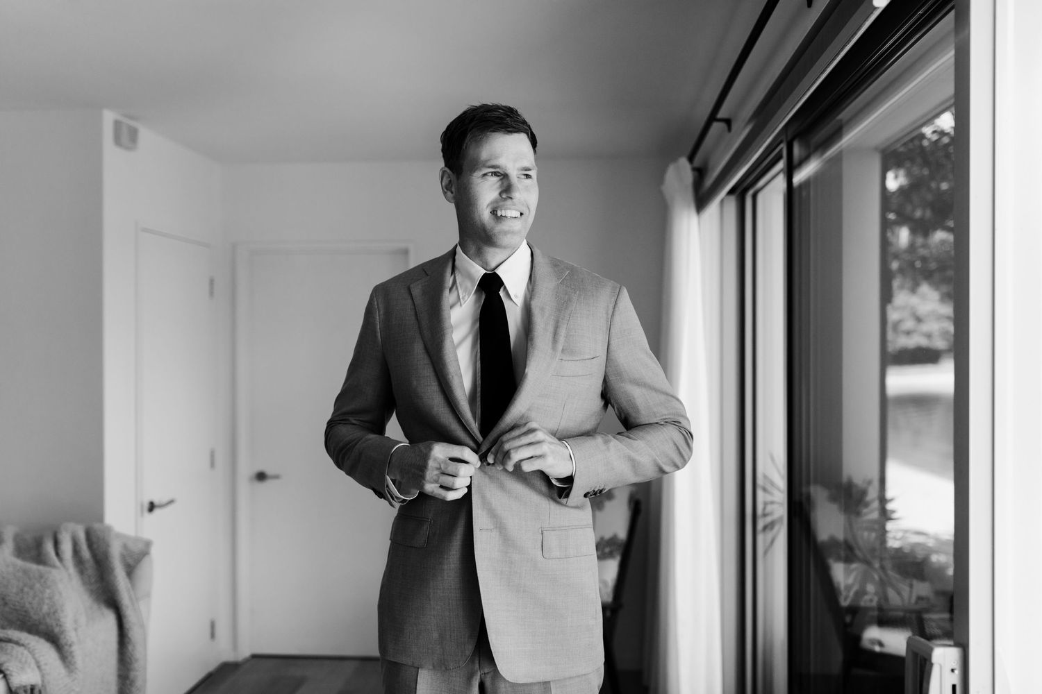 A person wearing a light gray suit jacket and tie smiles while getting ready.