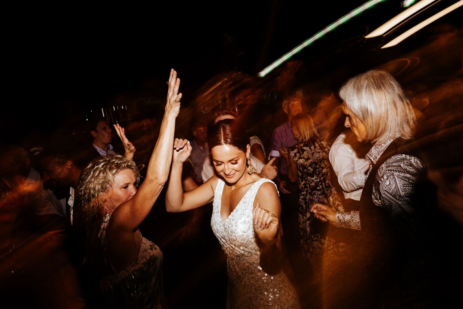 Wedding reception dance party scene with people dancing under warm lighting.