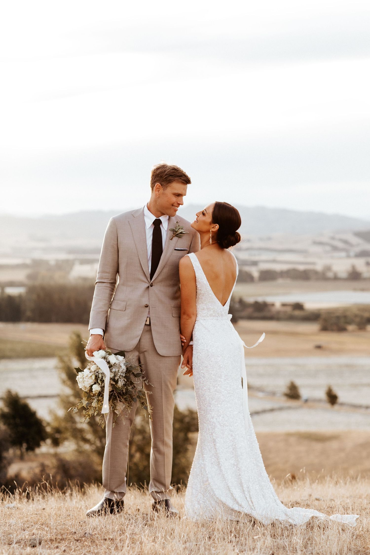 Elegant couple shares intimate moment on hilltop with scenic valley backdrop at their wedding.