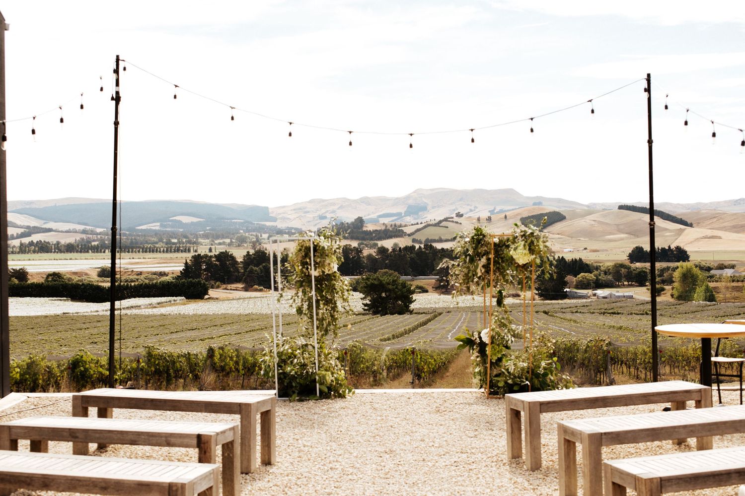 Outdoor wedding venue with rustic benches and string lights overlooking rolling hills.