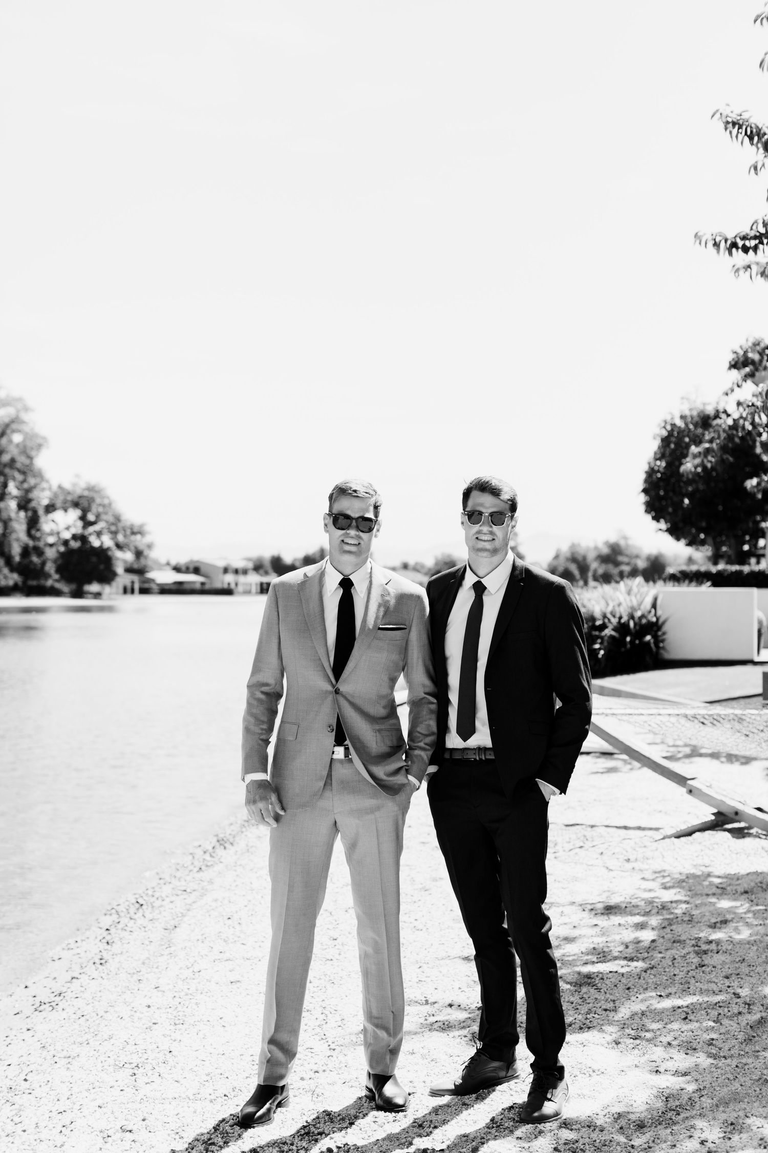 Two people in suits posing together outdoors on a sunny day.