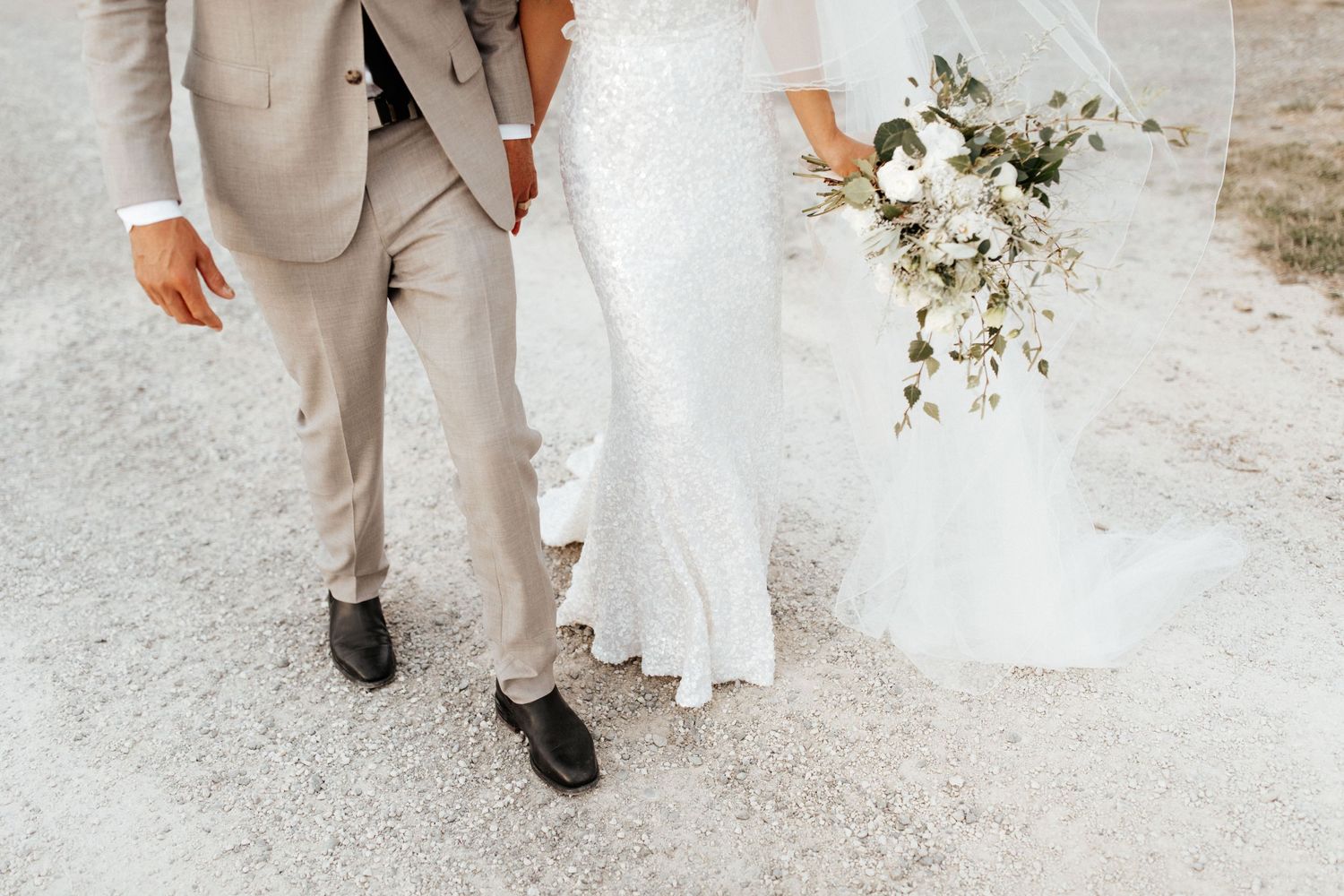 Close-up of bride and groom's formal attire showing light gray suit and white wedding dress with bouquet.