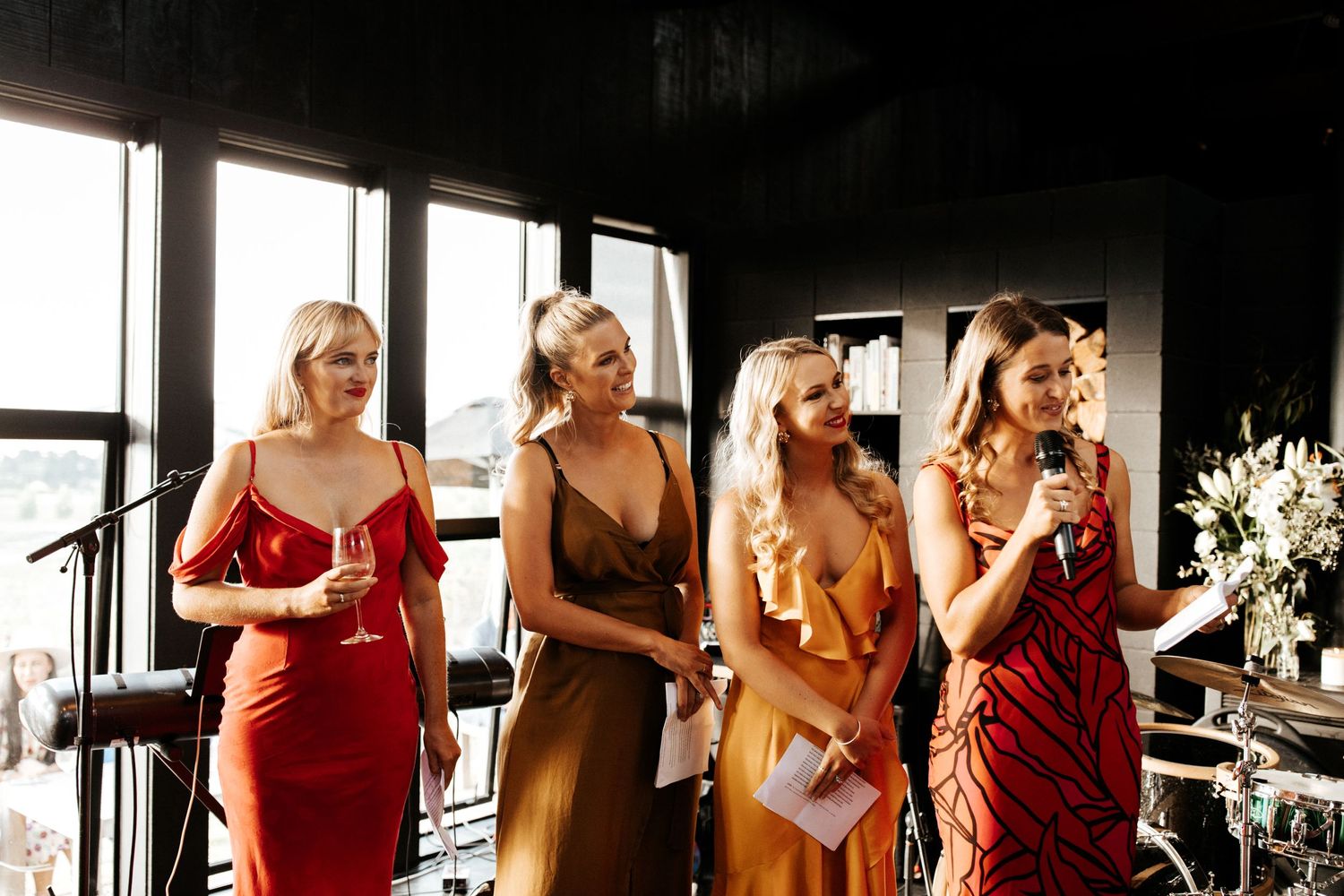 Bridesmaids in coordinating burgundy and rust colored dresses stand together at wedding venue.
