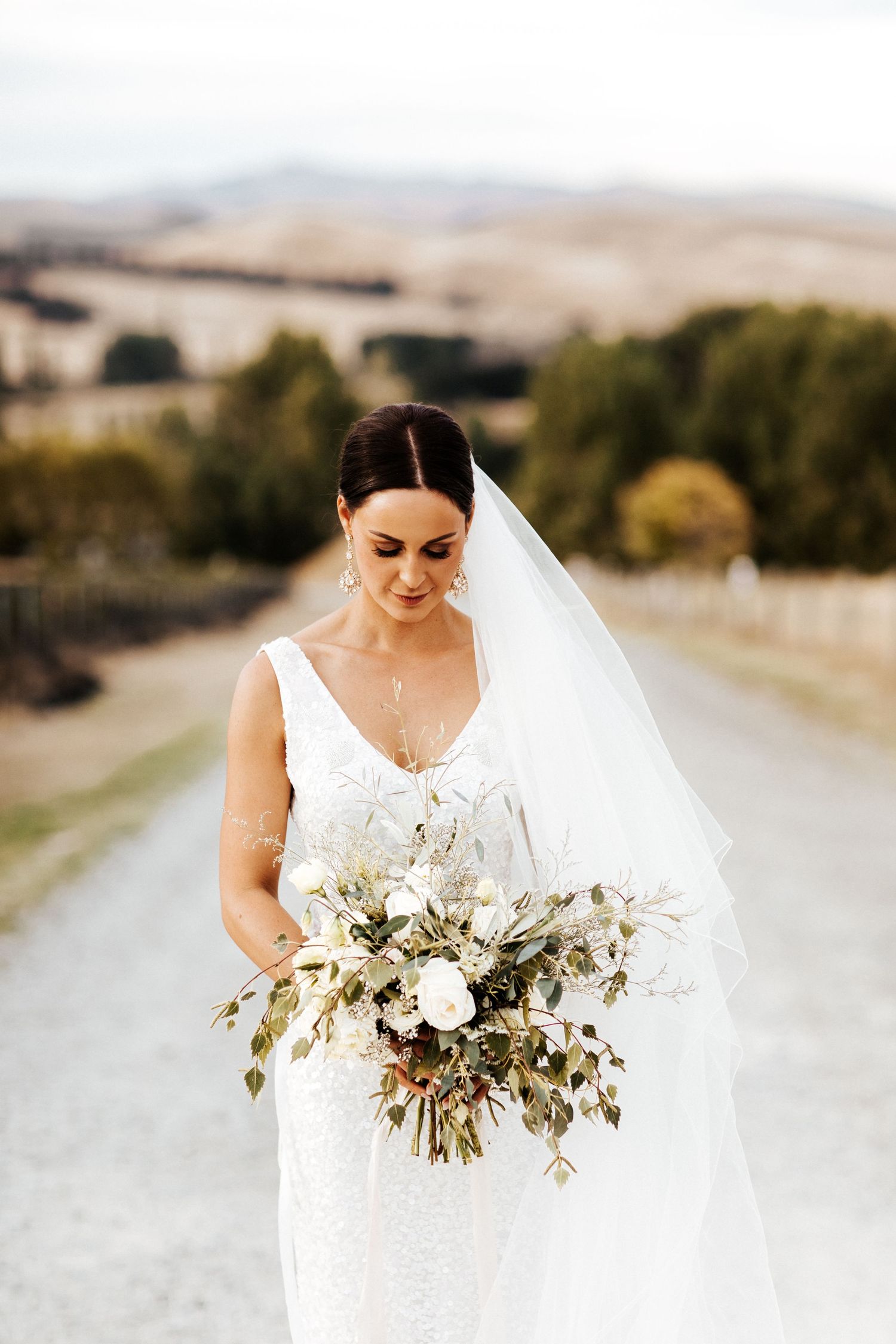 Bride holds elegant white and green bouquet while wearing classic v-neck gown and veil.