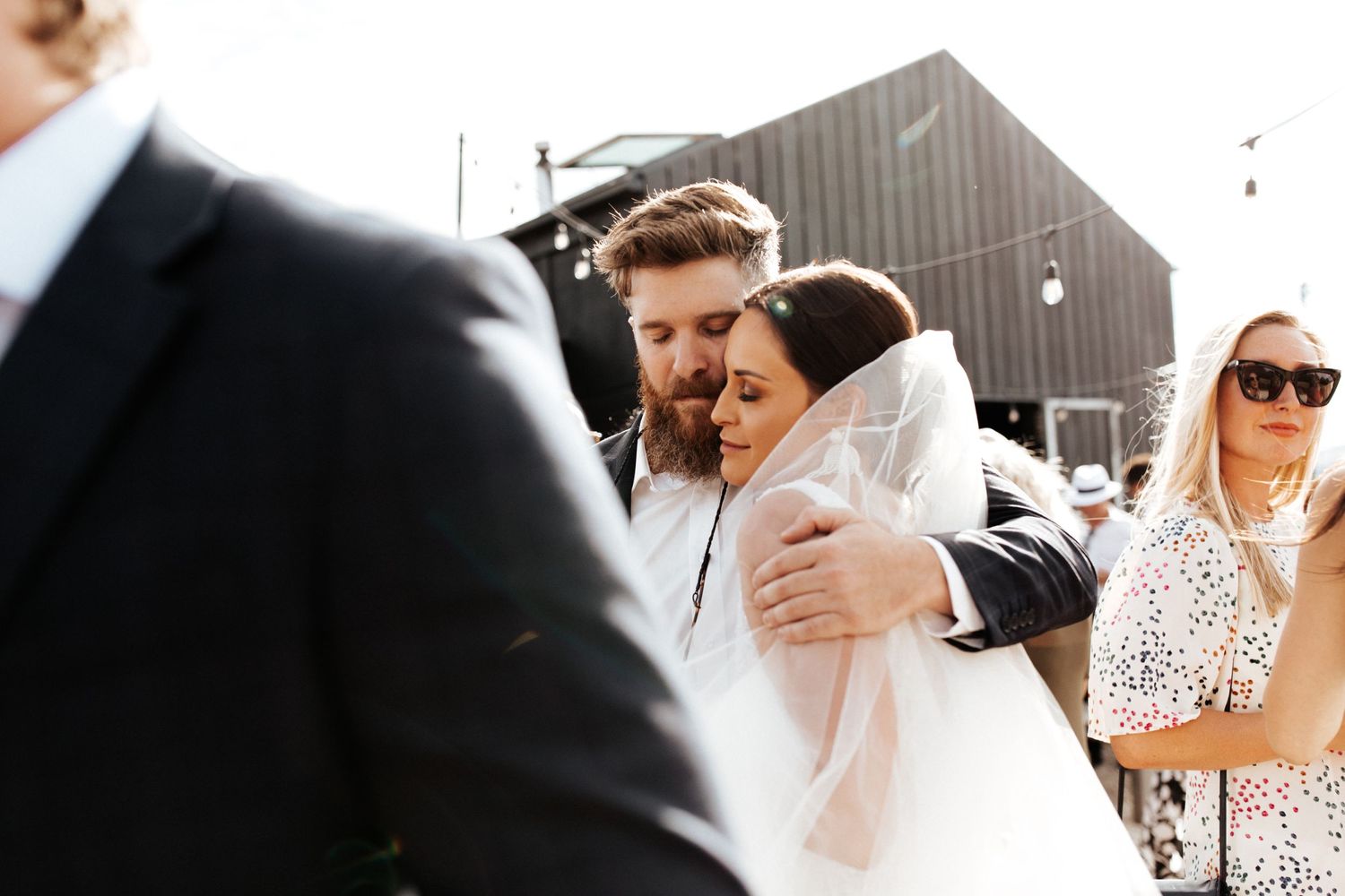 Intimate moment shared during an outdoor wedding with string lights and modern barn backdrop.