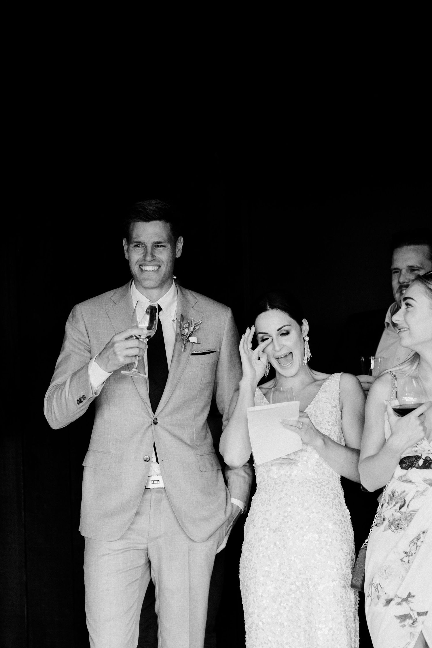 Black and white photo of wedding celebration with guests enjoying drinks and laughter.