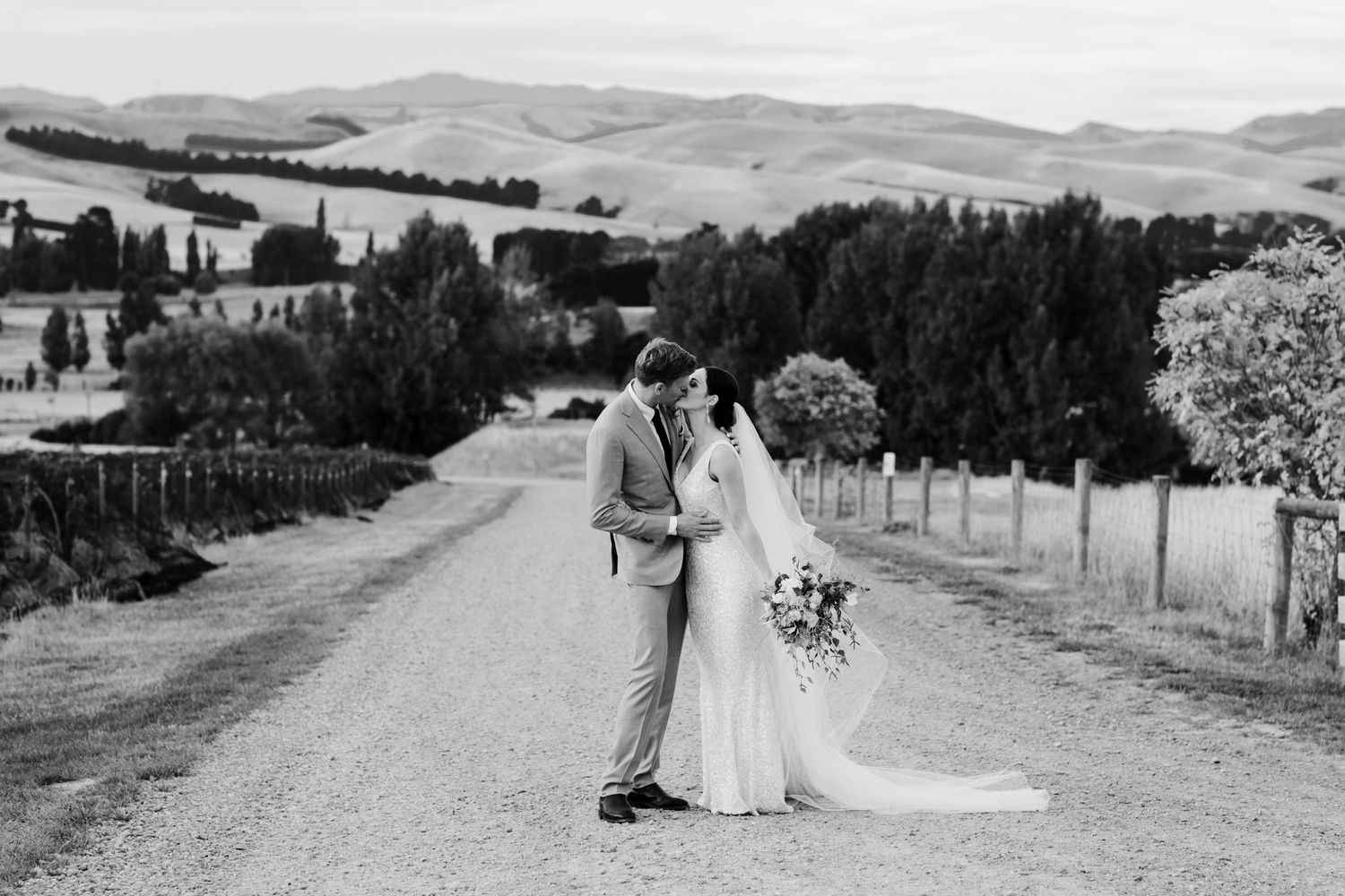 A romantic wedding couple poses on a rural country road with rolling hills in the background.