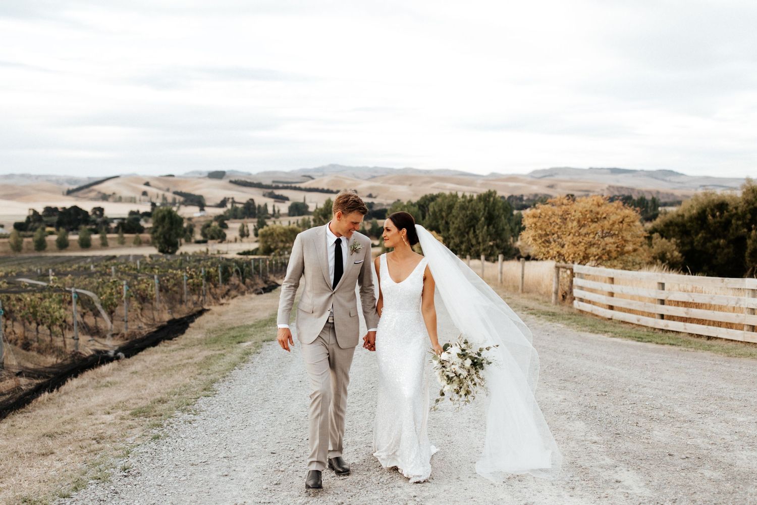 Wedding couple walking along a country road surrounded by scenic farmland and rolling hills.