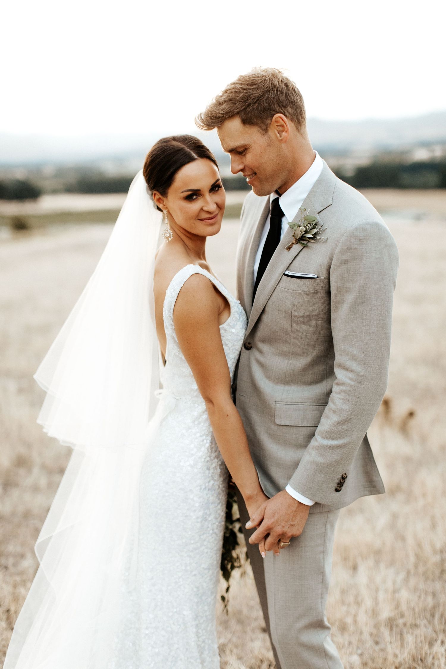 Romantic wedding portrait in golden field with mountains in background.