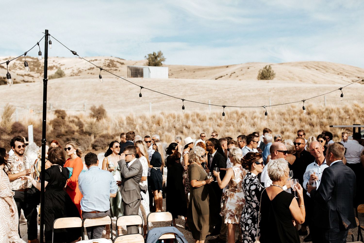 Wedding guests gather for an outdoor ceremony against a backdrop of rolling desert hills.