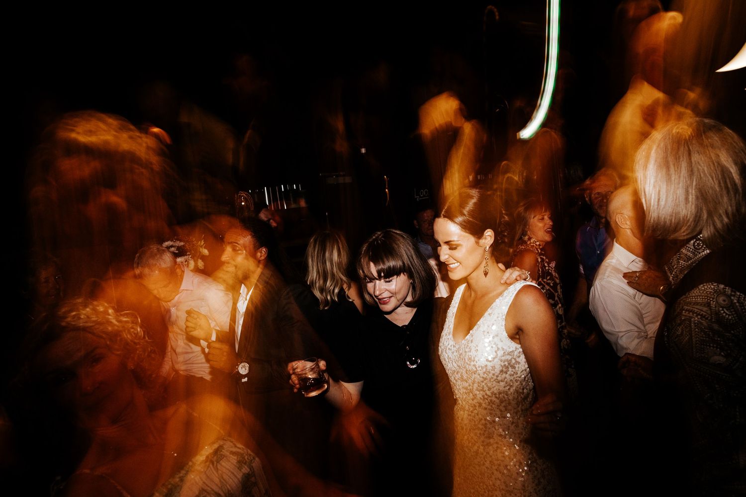Energetic dance floor moment at a wedding reception with motion blur and ambient lighting.