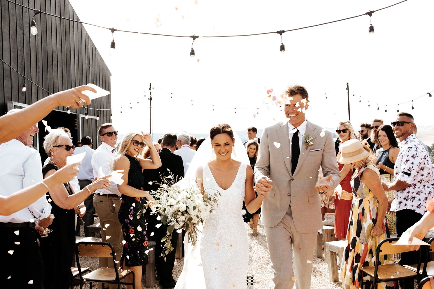 Newlyweds walk down the aisle while guests throw confetti during their outdoor celebration.