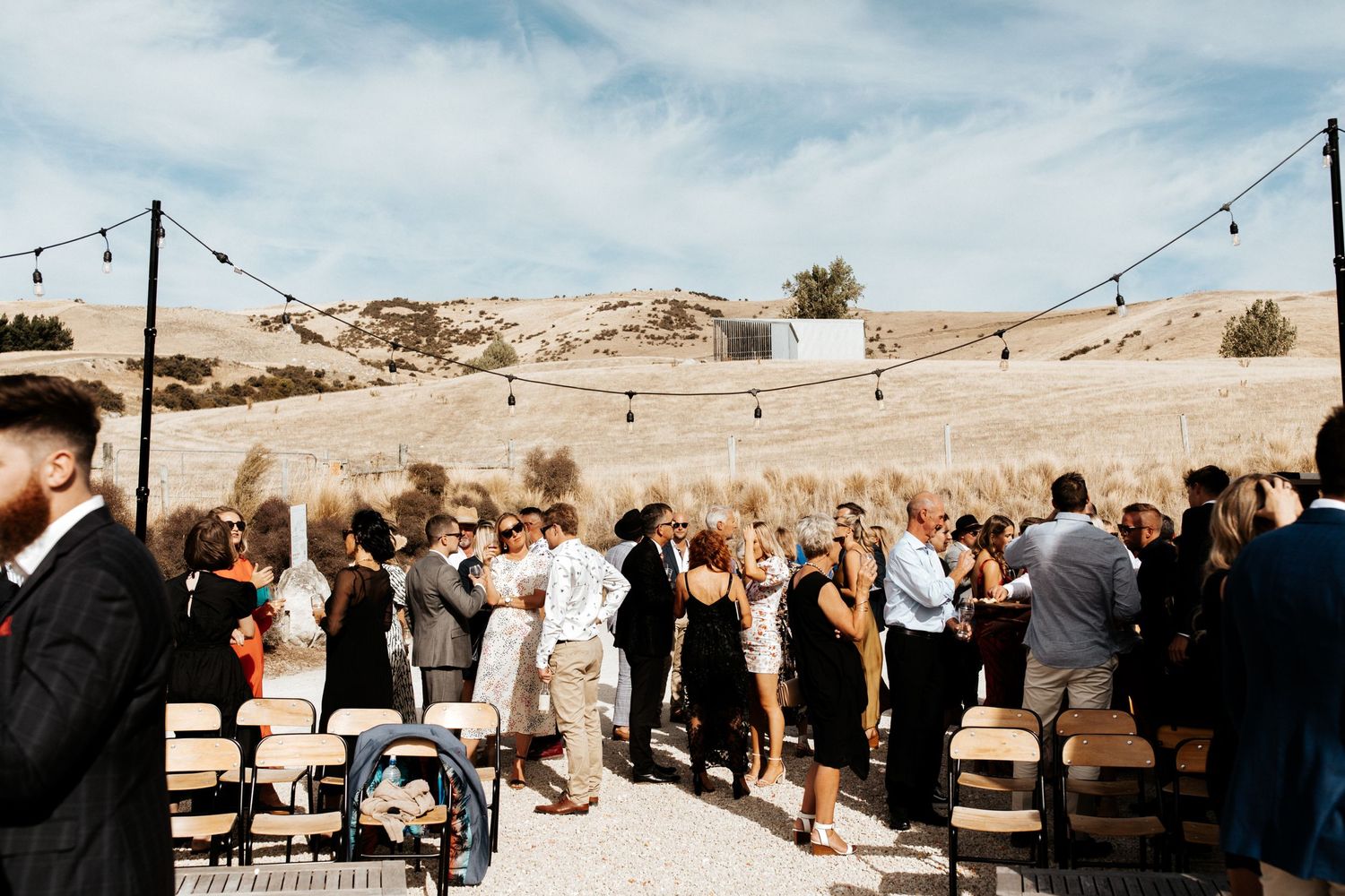 Wedding guests mingle during an outdoor ceremony with desert hills in the background.