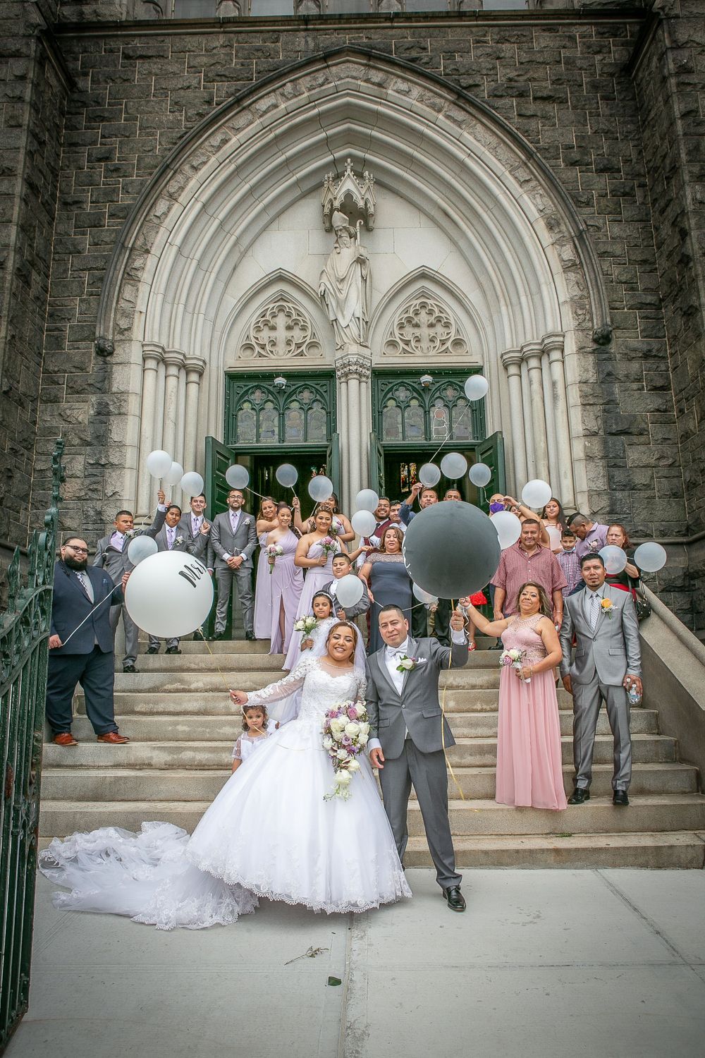 the bride and groom pose beside a church door with balloons, in the style of light magenta and light gray, nyc explosion