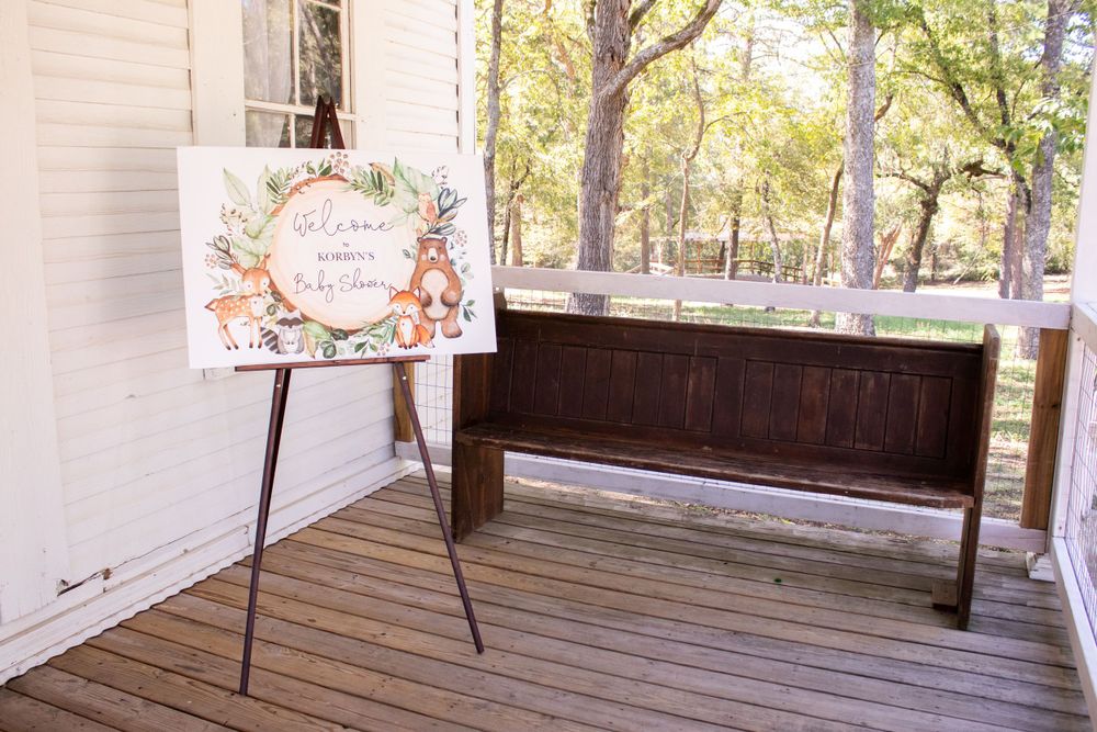 A covered outdoor porch with wooden benches and chairs arranged in rows faces a scenic wooded area.