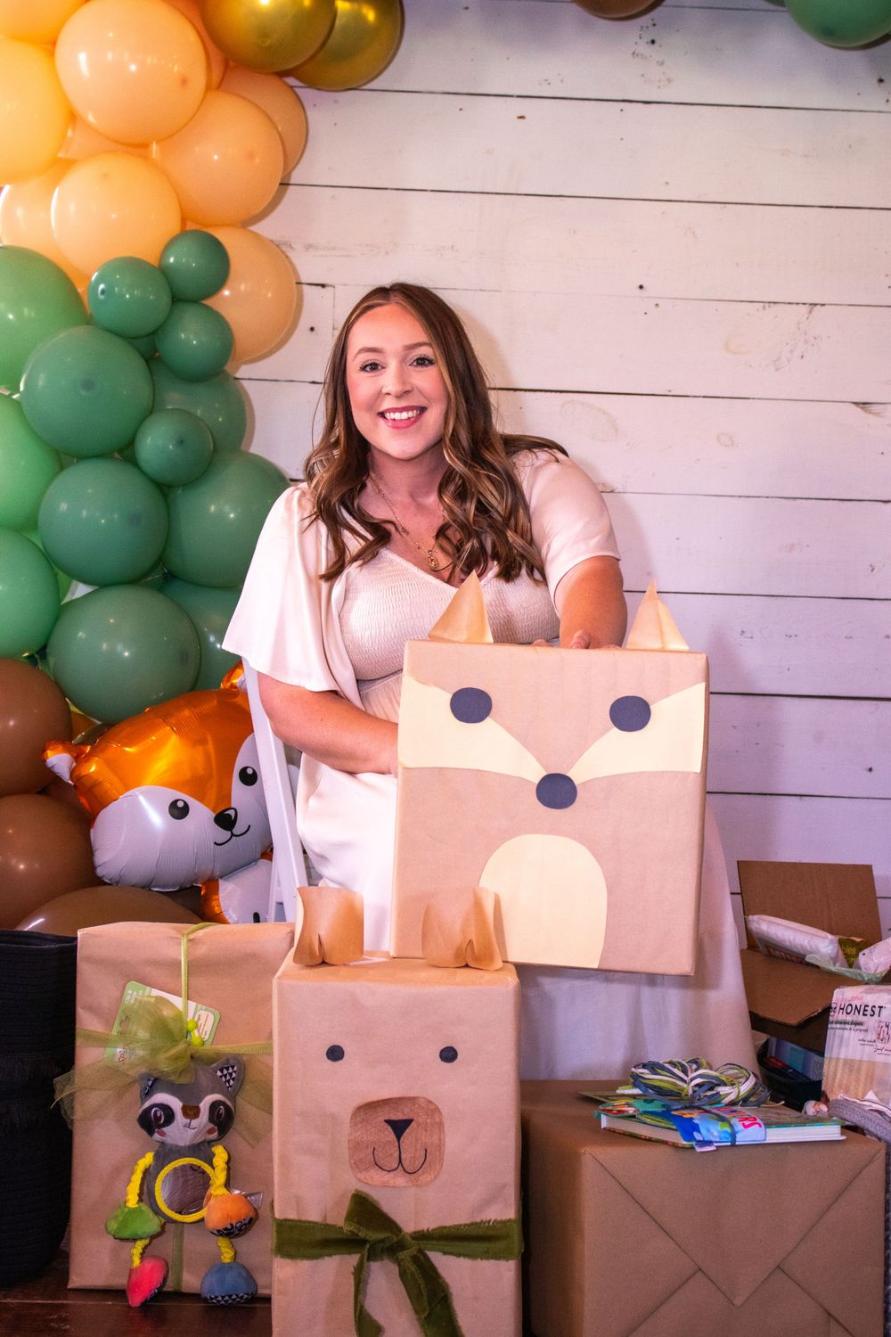 A sequence of photos showing someone creating a fun cardboard box costume with peach and green balloon decorations for a baby shower.