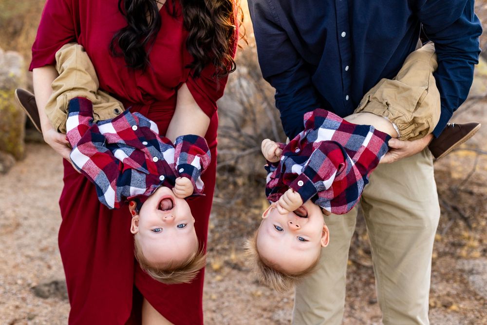 Couple holding two babies wearing matching plaid outfits during an outdoor photoshoot.