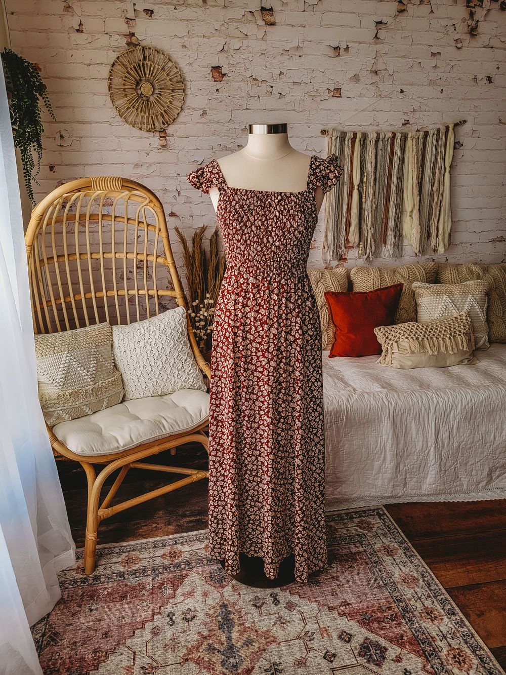 Dark floral smocked bodice maxi dress with cap sleeves on a mannequin in a boho decorated interior.