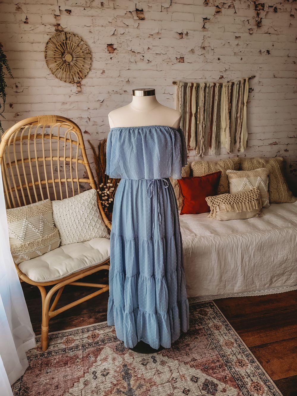Dusty blue off-shoulder tiered maxi dress with drawstring waist on a mannequin in a boho styled room.